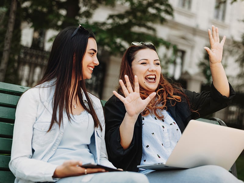 two women sit on bench with laptop