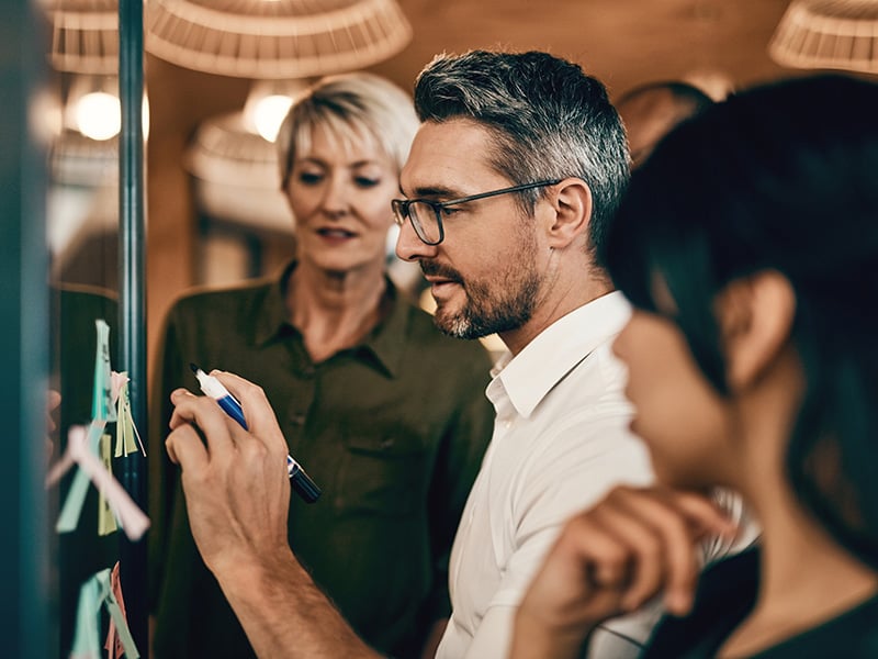 Man writes at whiteboard as two women look on