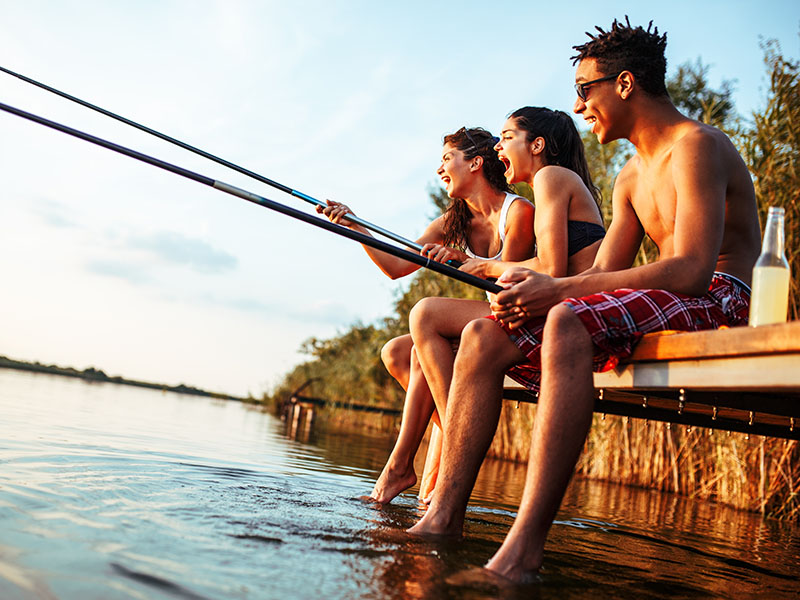 Three people holding fishing rods sitting on a dock