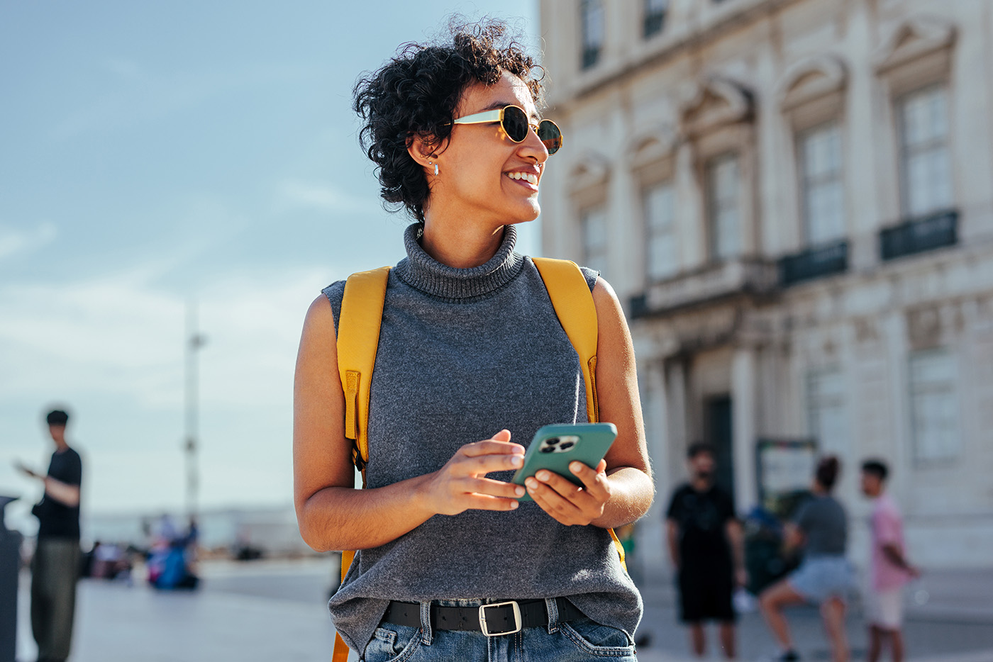 a woman walking with her phone in her hands wearing sunglasses and a yellow backpack