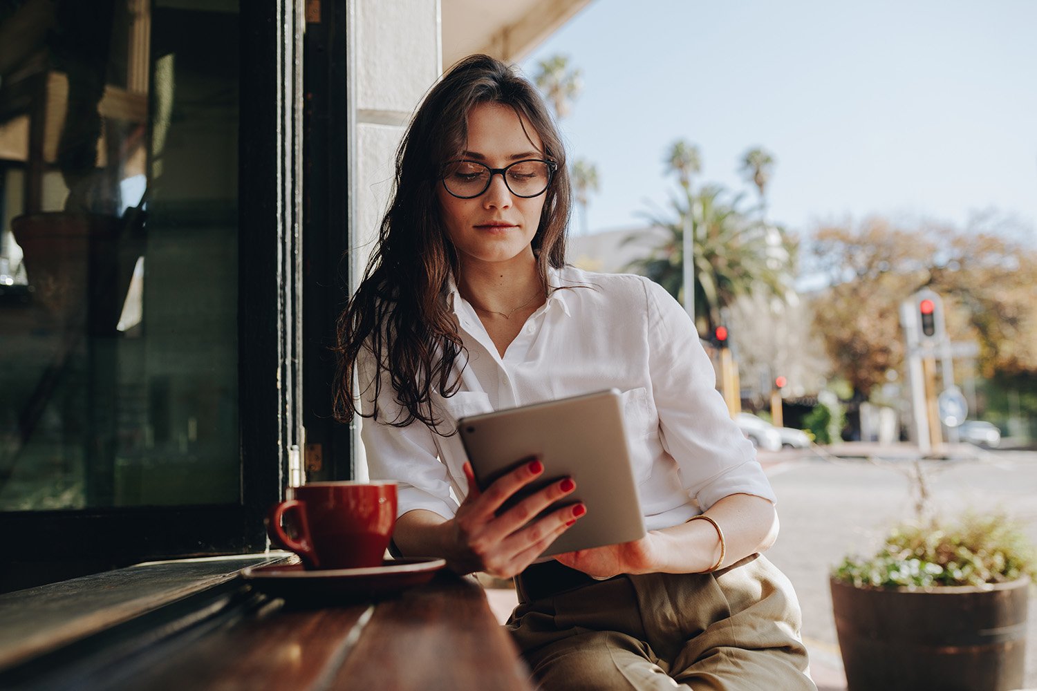 a woman sitting at a cafe on her tablet with a mug of coffee