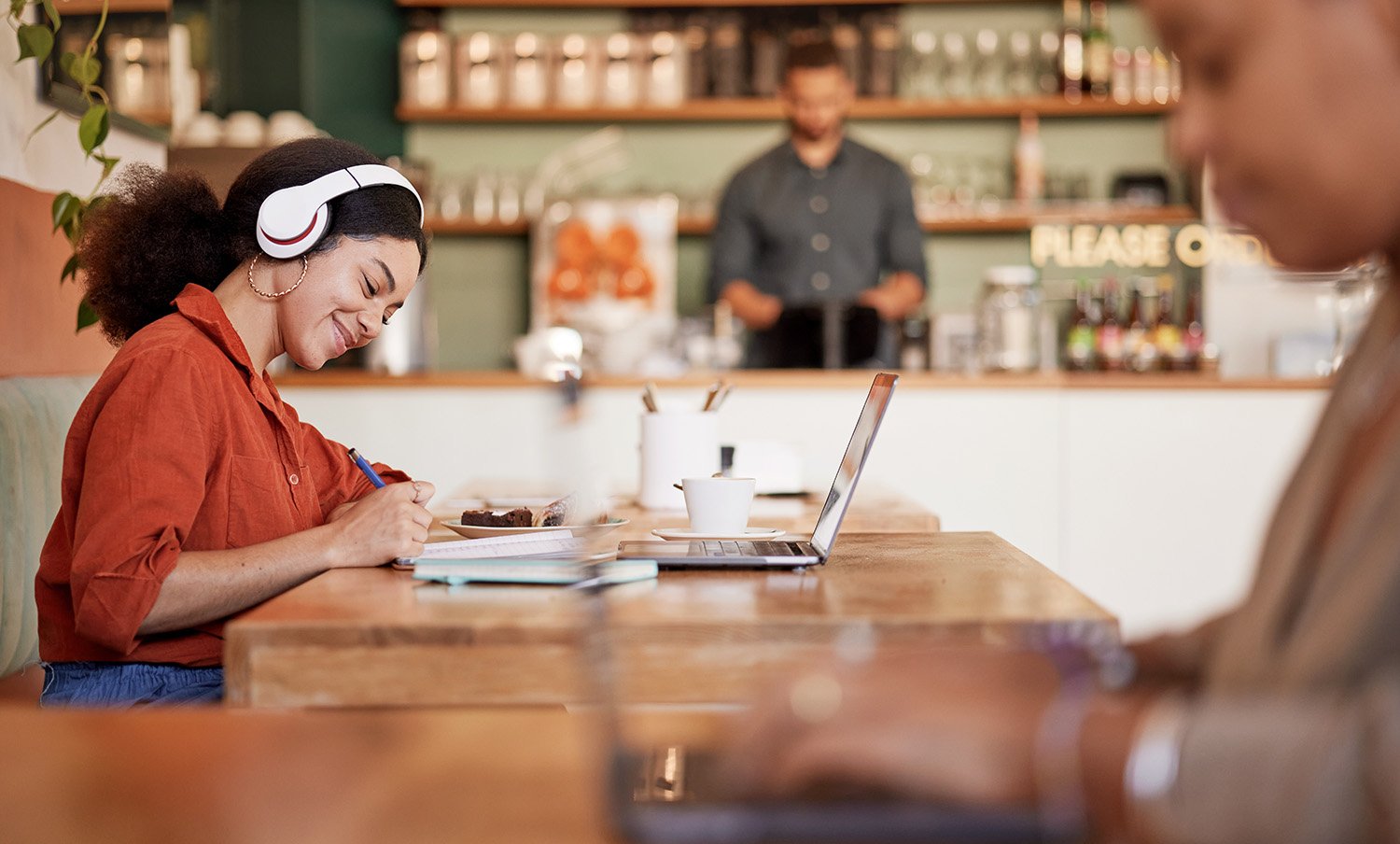 a woman with headphones on sits at a cafe table writing