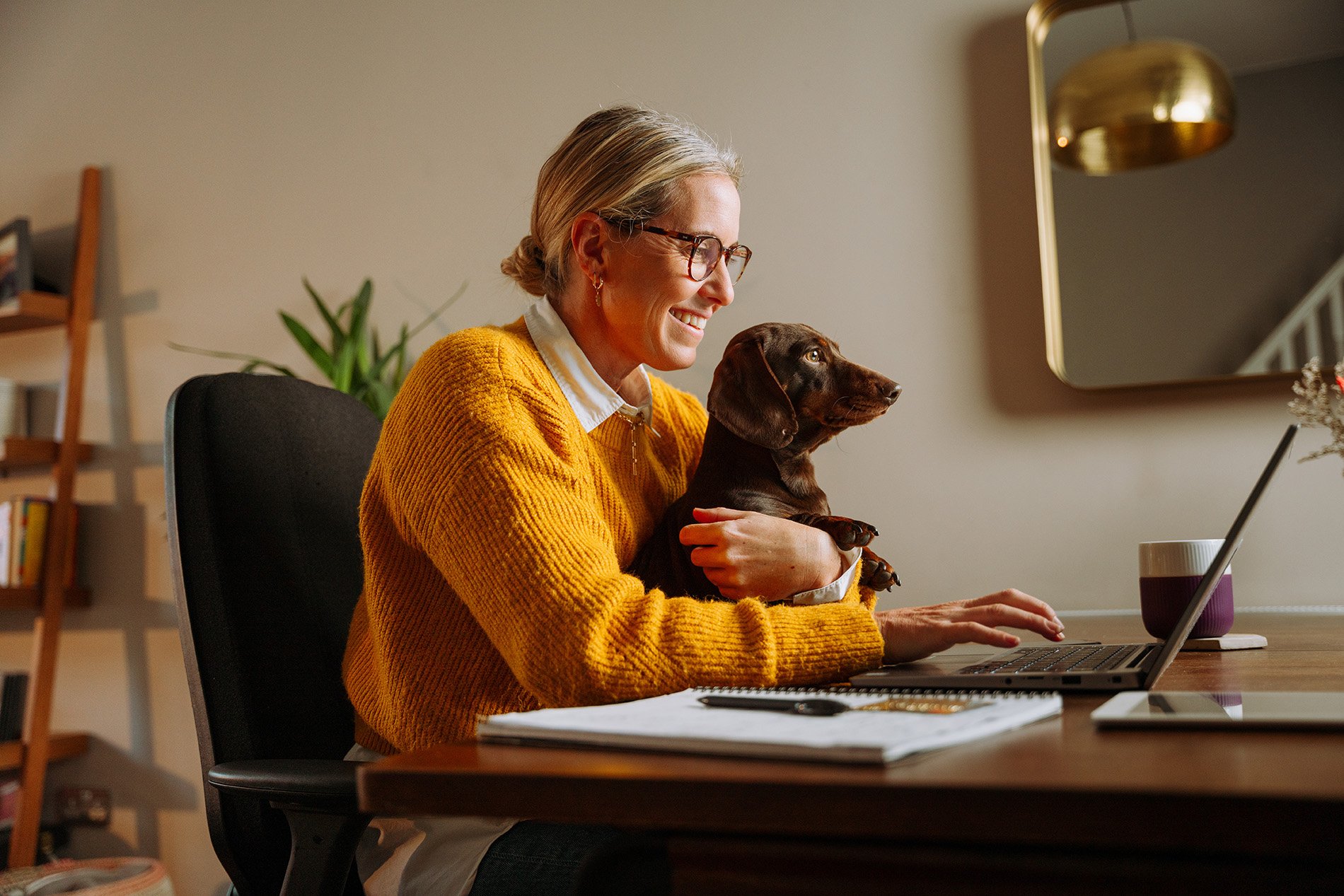 A woman sitting at her computer with a dog in her lap