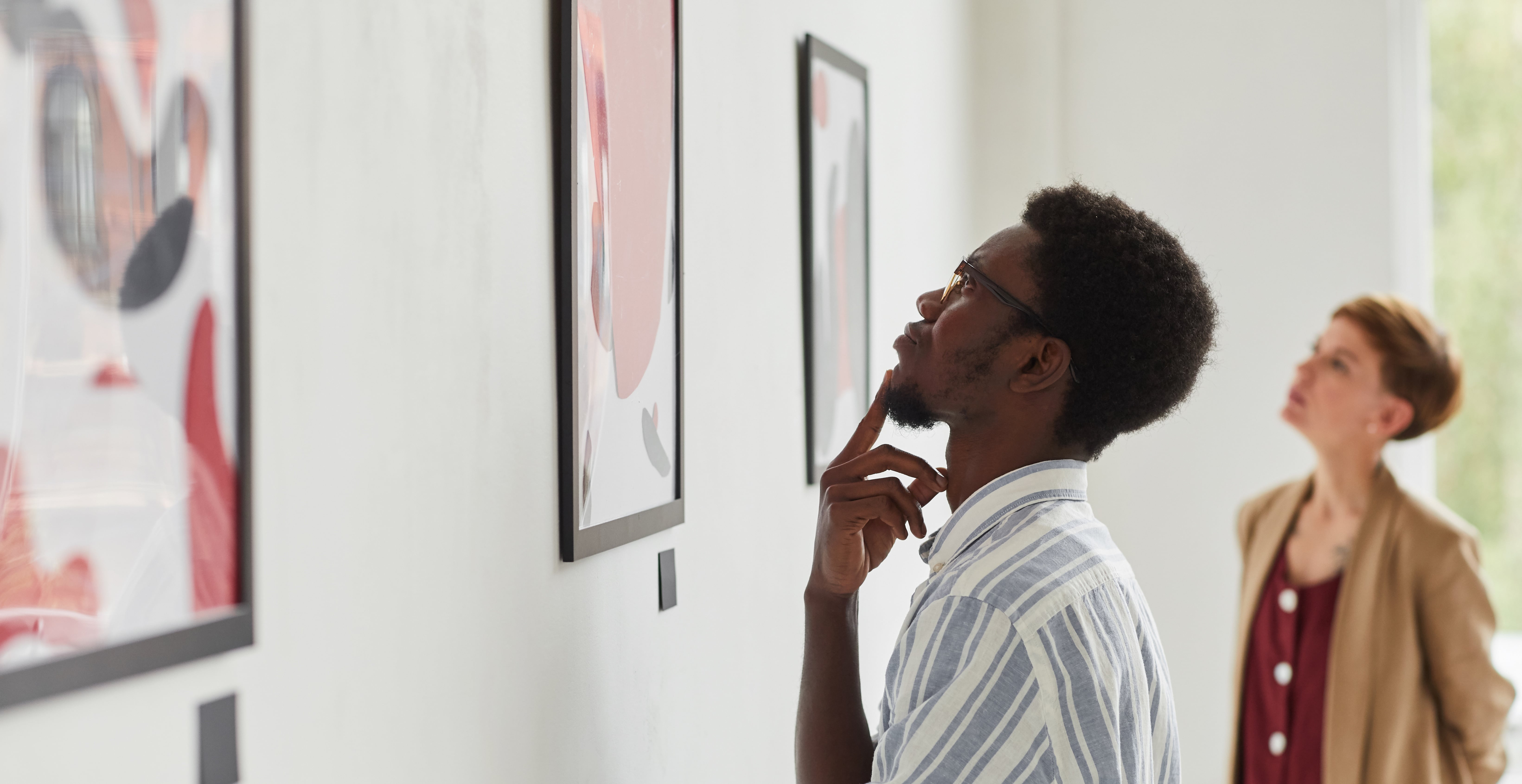 Two people look thoughtful as they gaze at art hanging on a gallery wall. 