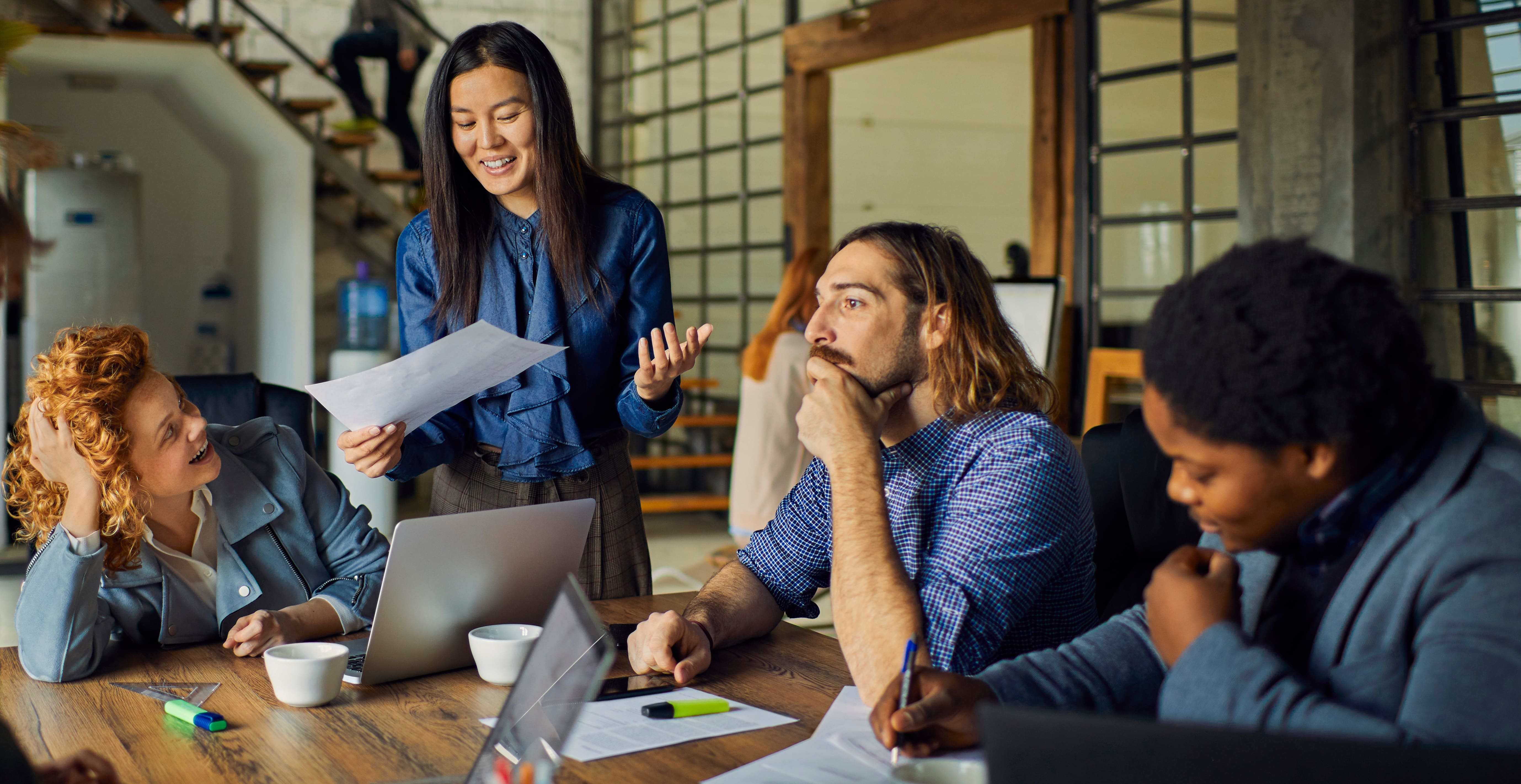 A group of young coworkers talk around a conference table in a cool, contemporary office.