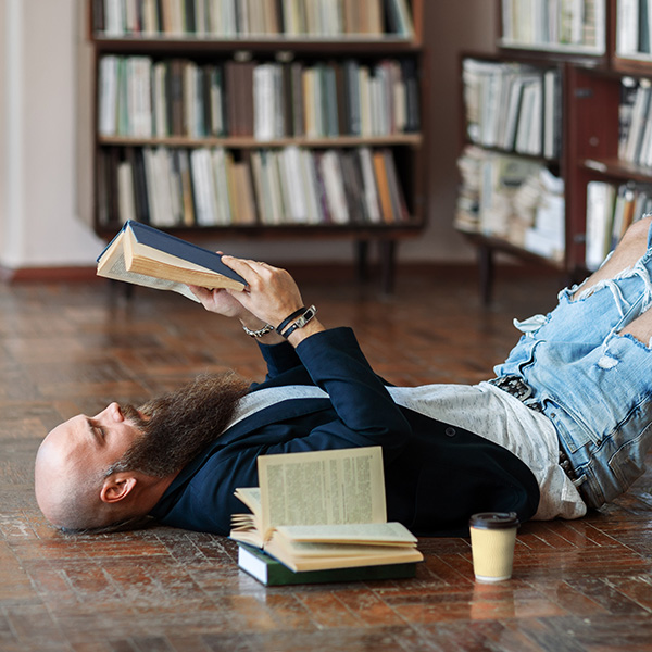 A man lies on the floor of a library while reading a book