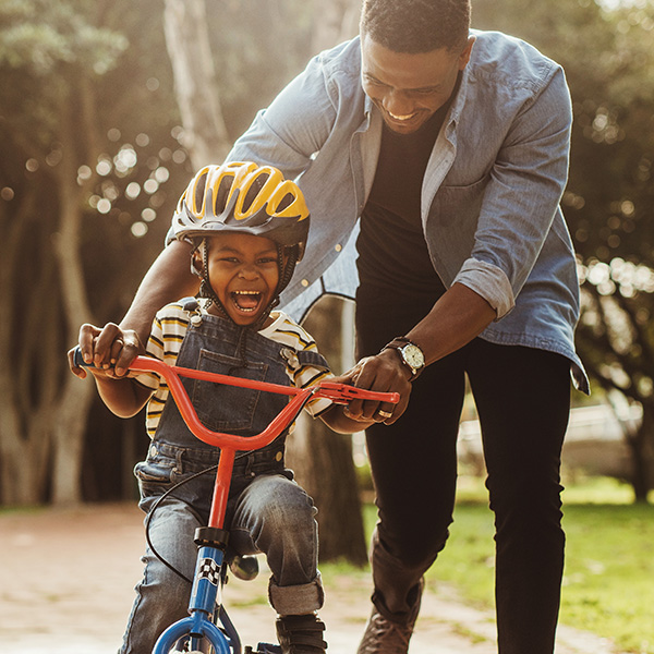 A young child and father laugh while the child rides a bike