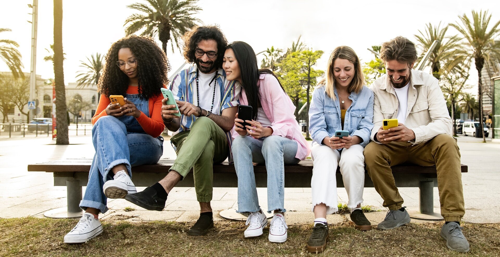 A group of young adults sits on a bench, each one holding a smartphone. 