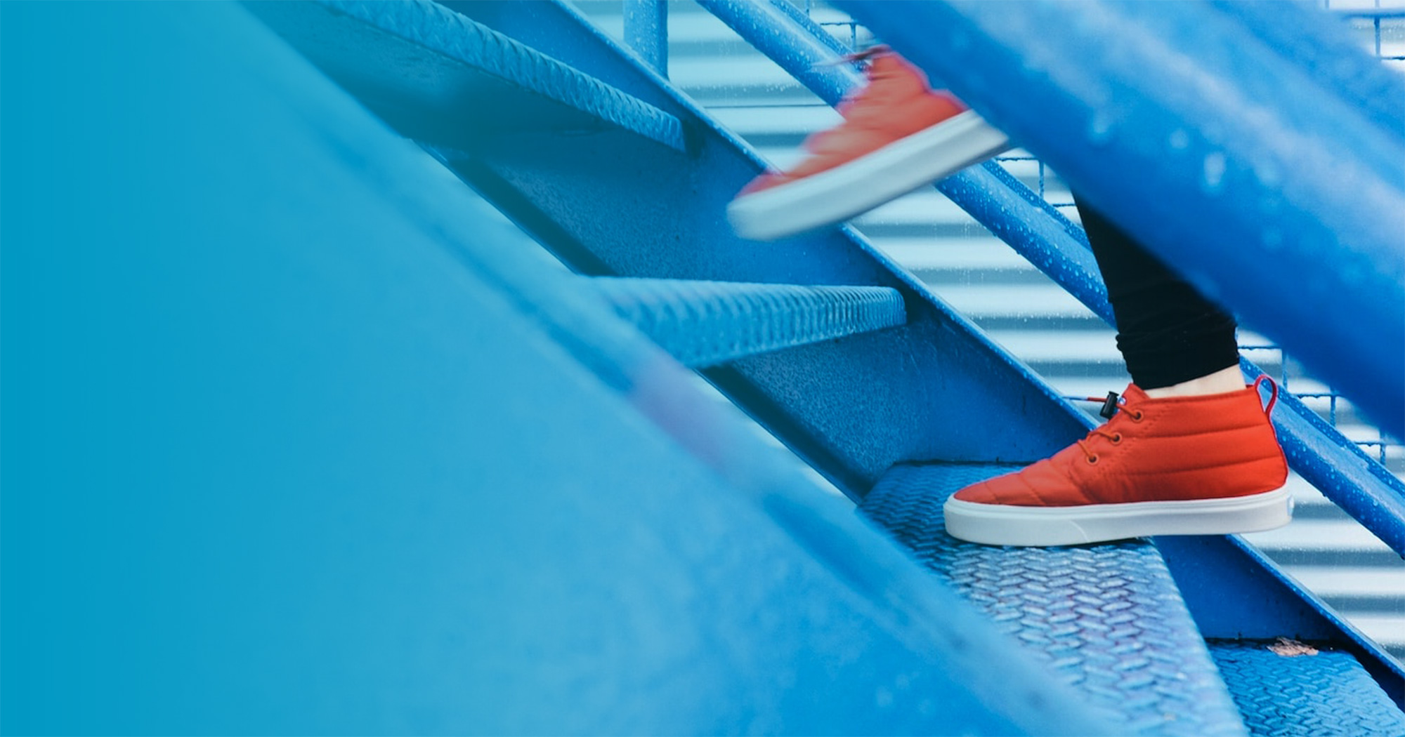 Person with orange sneakers climbing up a blue metal staircase