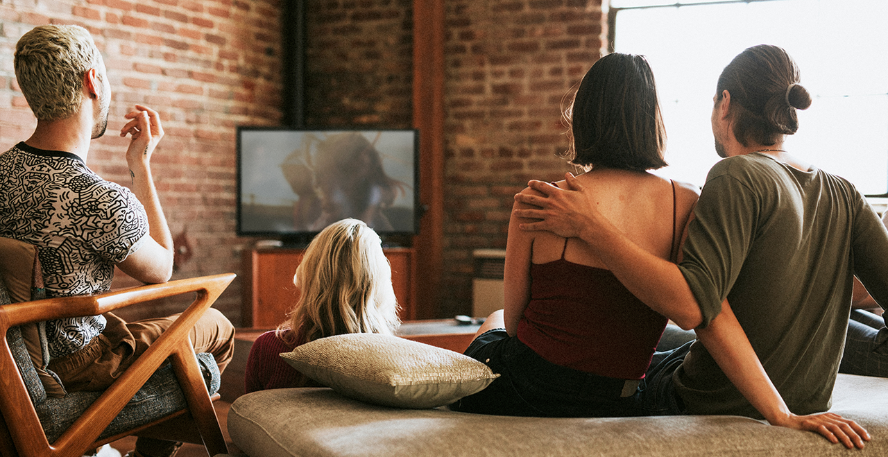 Four people are hanging out and watching a TV screen.