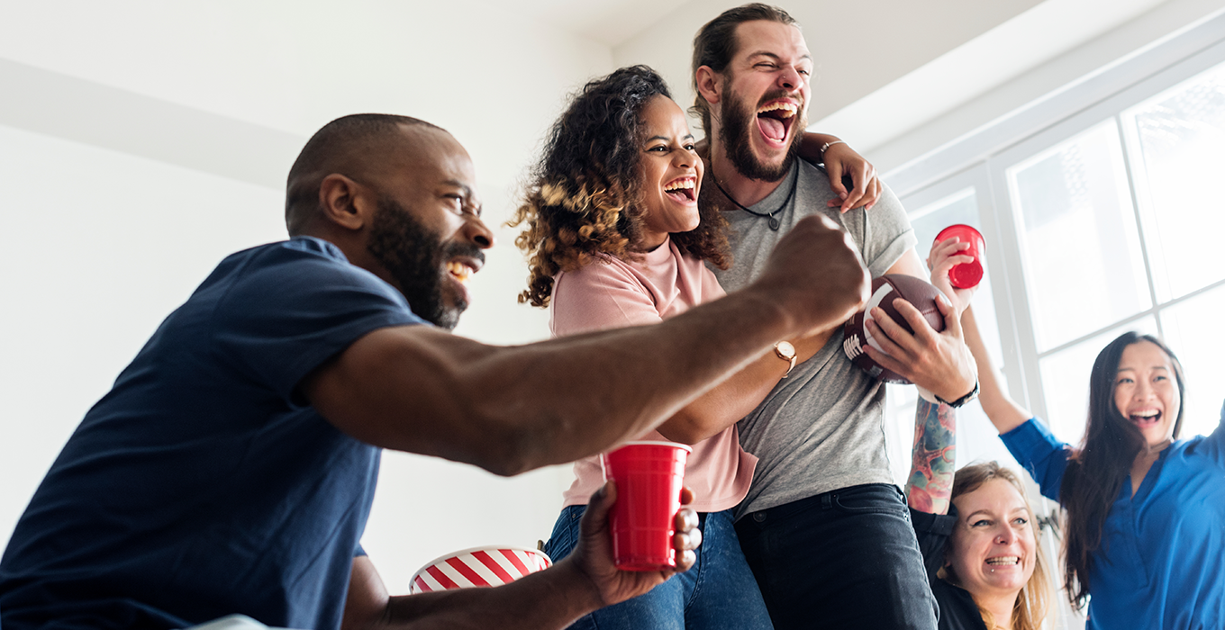 A group of young adults excitedly gesture as they watch a TV screen out of frame.